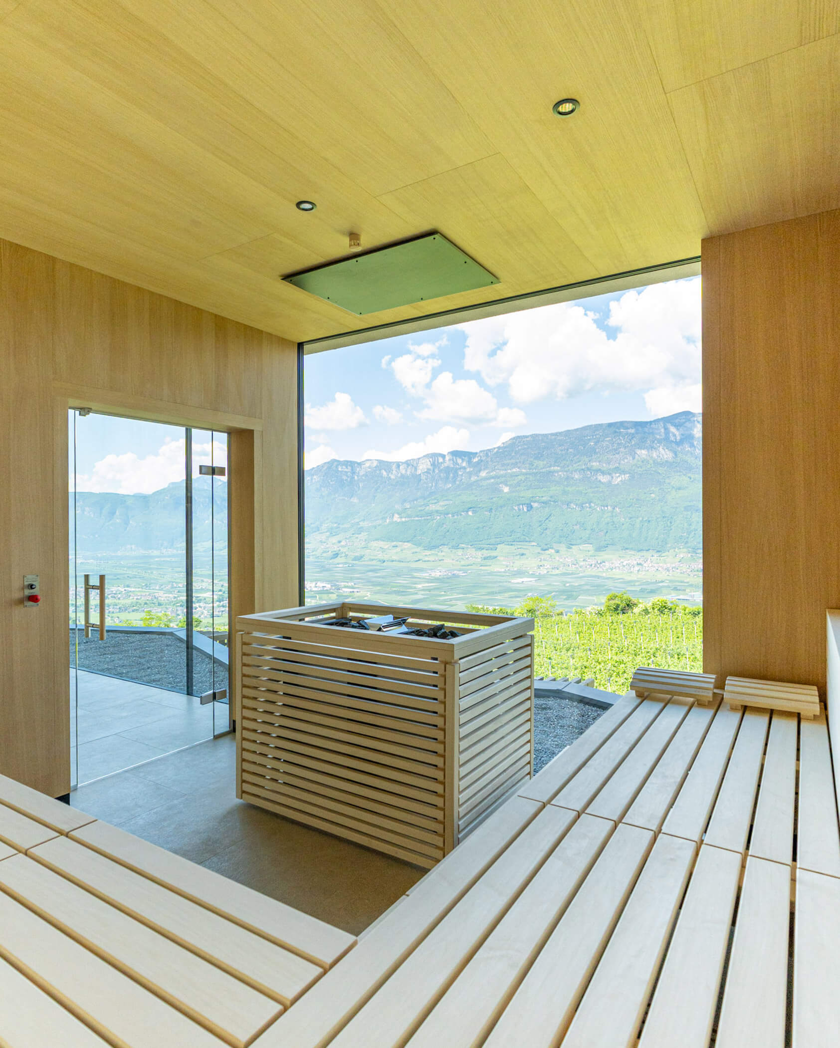 Modern wooden sauna with a large window overlooking green hills and distant mountains under a blue sky. - Hotel Tenz