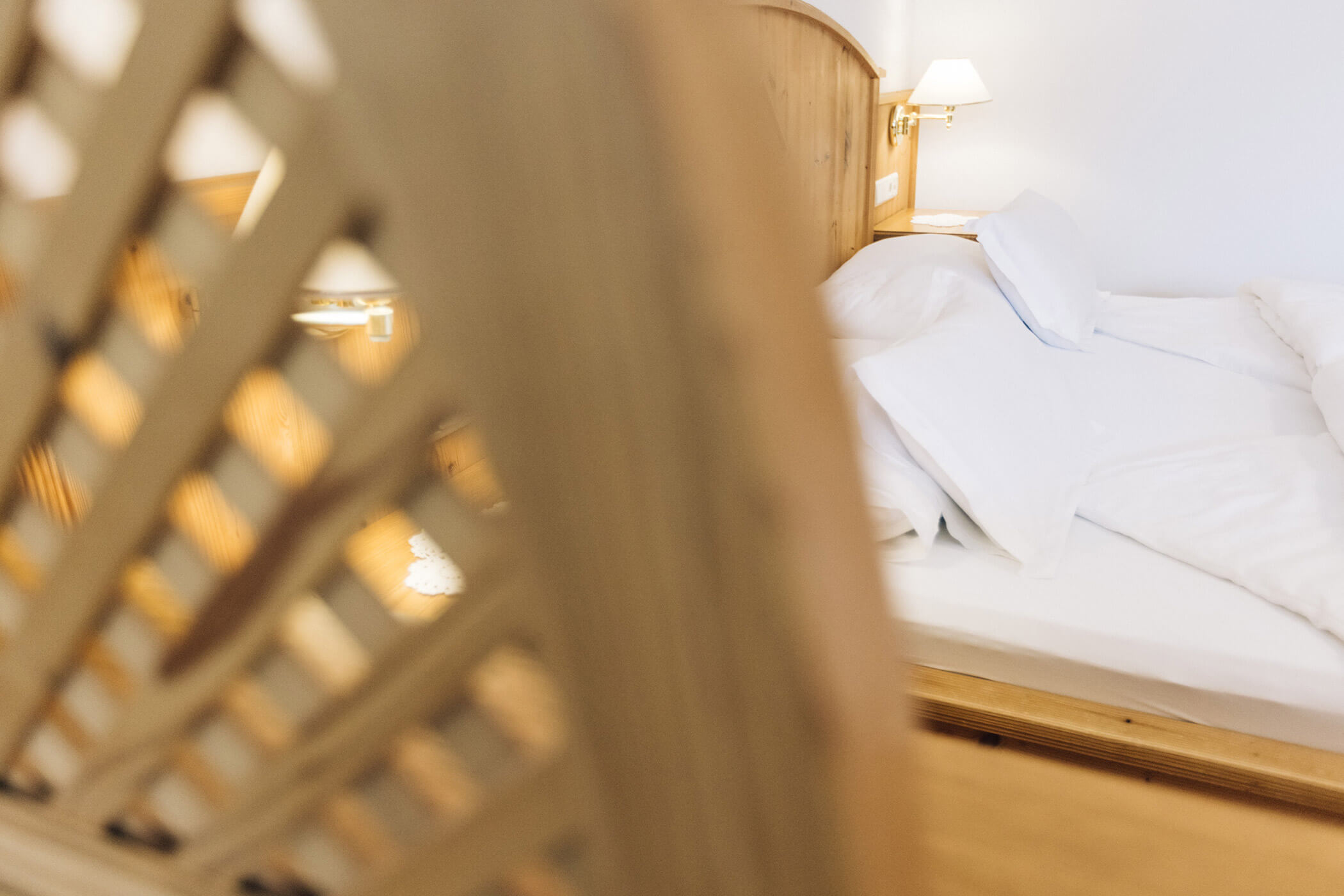 Bed with white pillows and sheets, partially obscured by a wooden lattice in the foreground. - Hotel Tenz