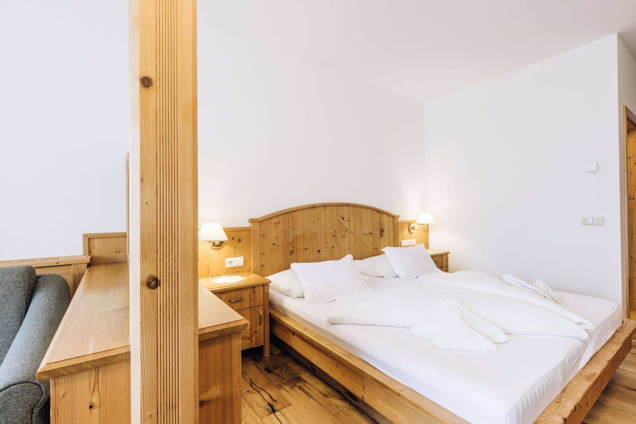Cozy hotel room with wooden furniture, double bed, white bedding, bedside lamps, and a gray sofa. - Hotel Tenz