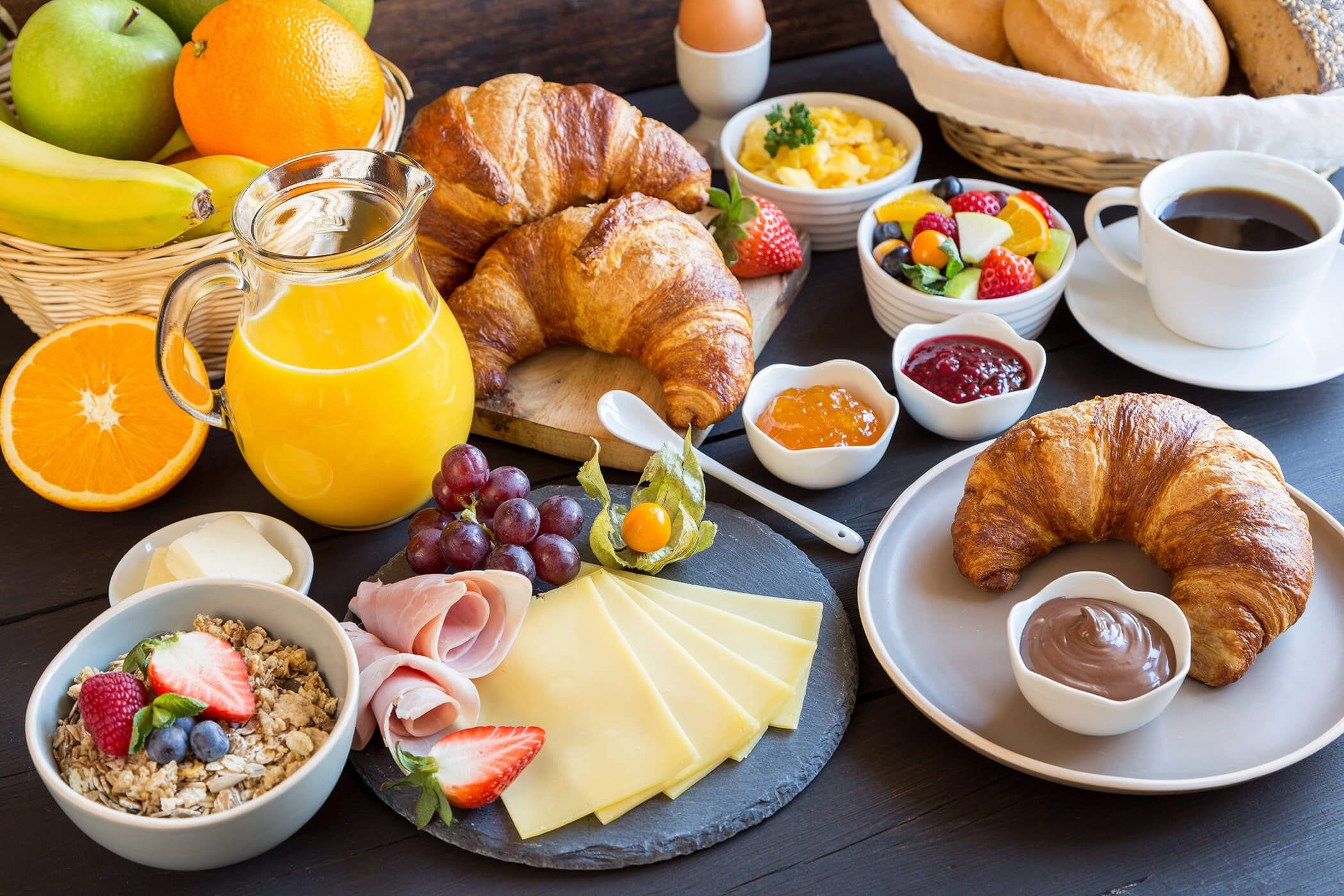 Breakfast spread with croissants, cheese, ham, fruit, granola, orange juice, coffee, and jams on a table. - Hotel Tenz
