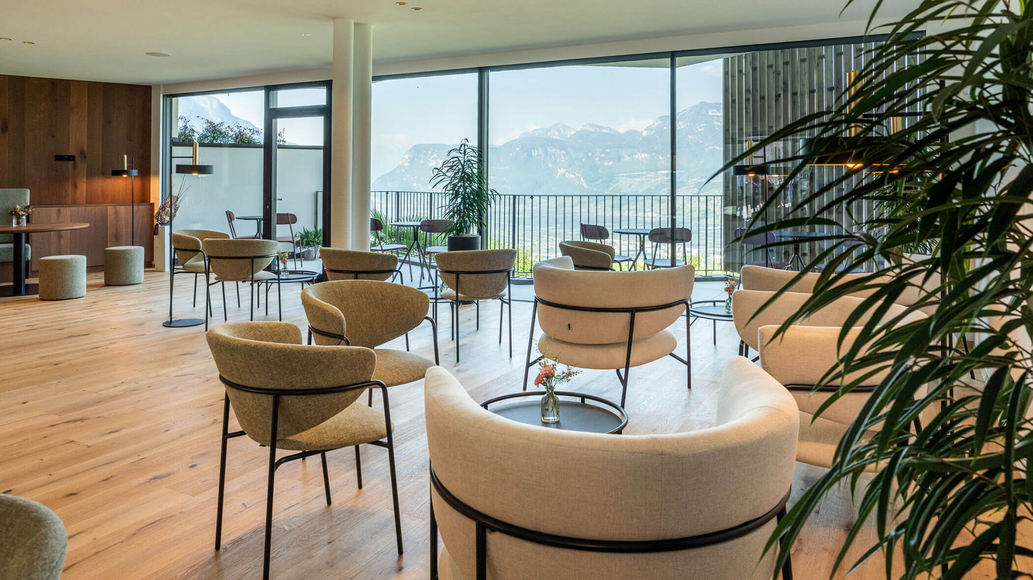 Moderne Lounge mit beigen Stühlen und Tischen, großen Fenstern, Bergblick und Zimmerpflanzen. - Hotel Tenz
