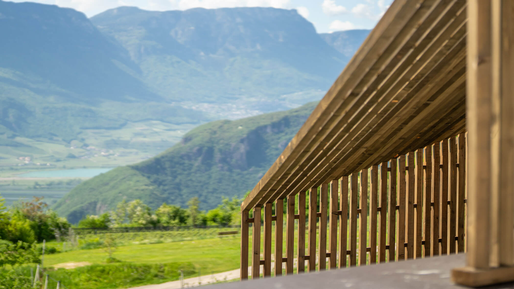Wooden slatted structure with mountains and green landscape in the background on a sunny day. - Hotel Tenz