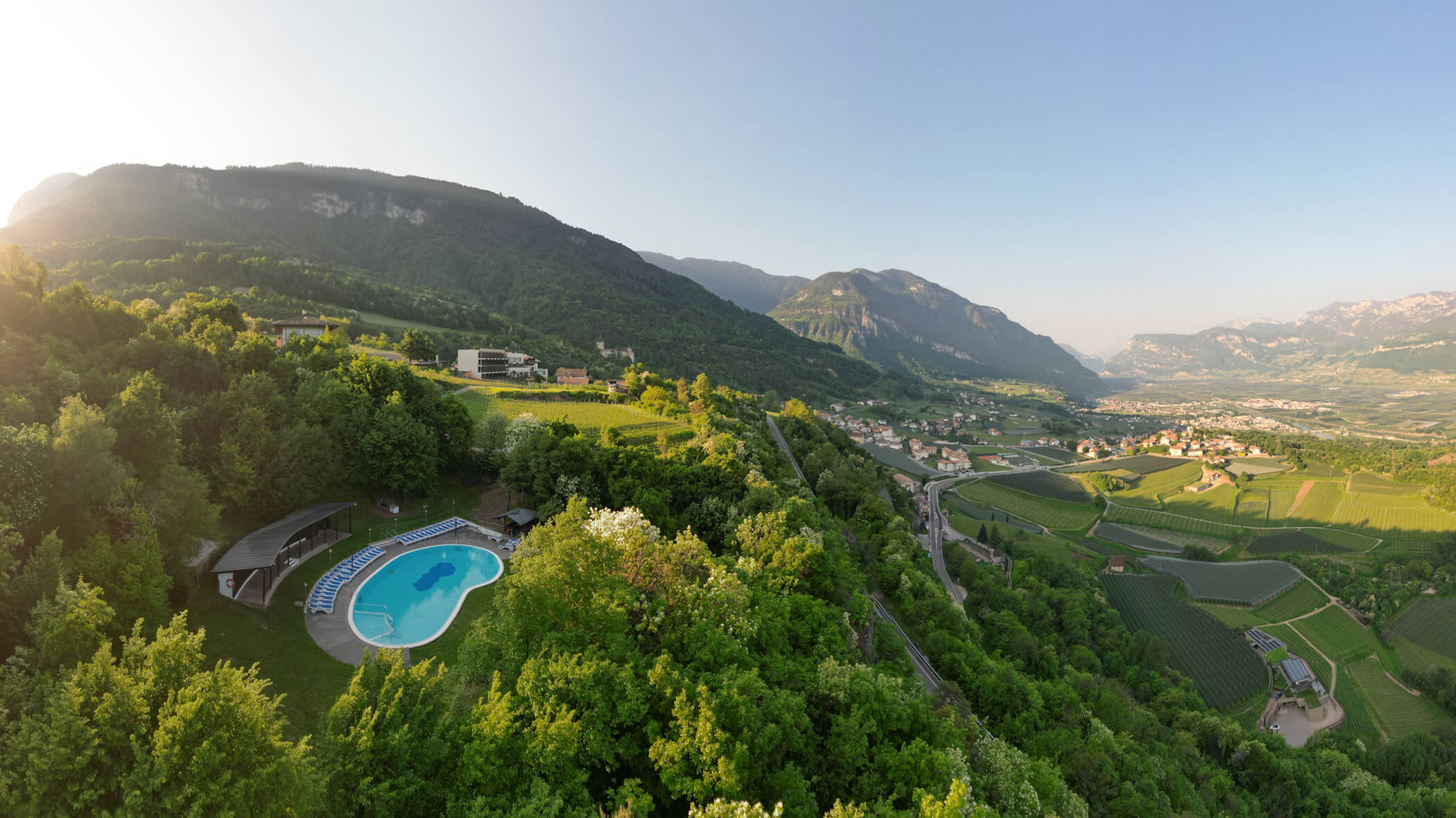 Aerial view of a hillside pool surrounded by lush greenery, with mountains and a valley in the background. - Hotel Tenz