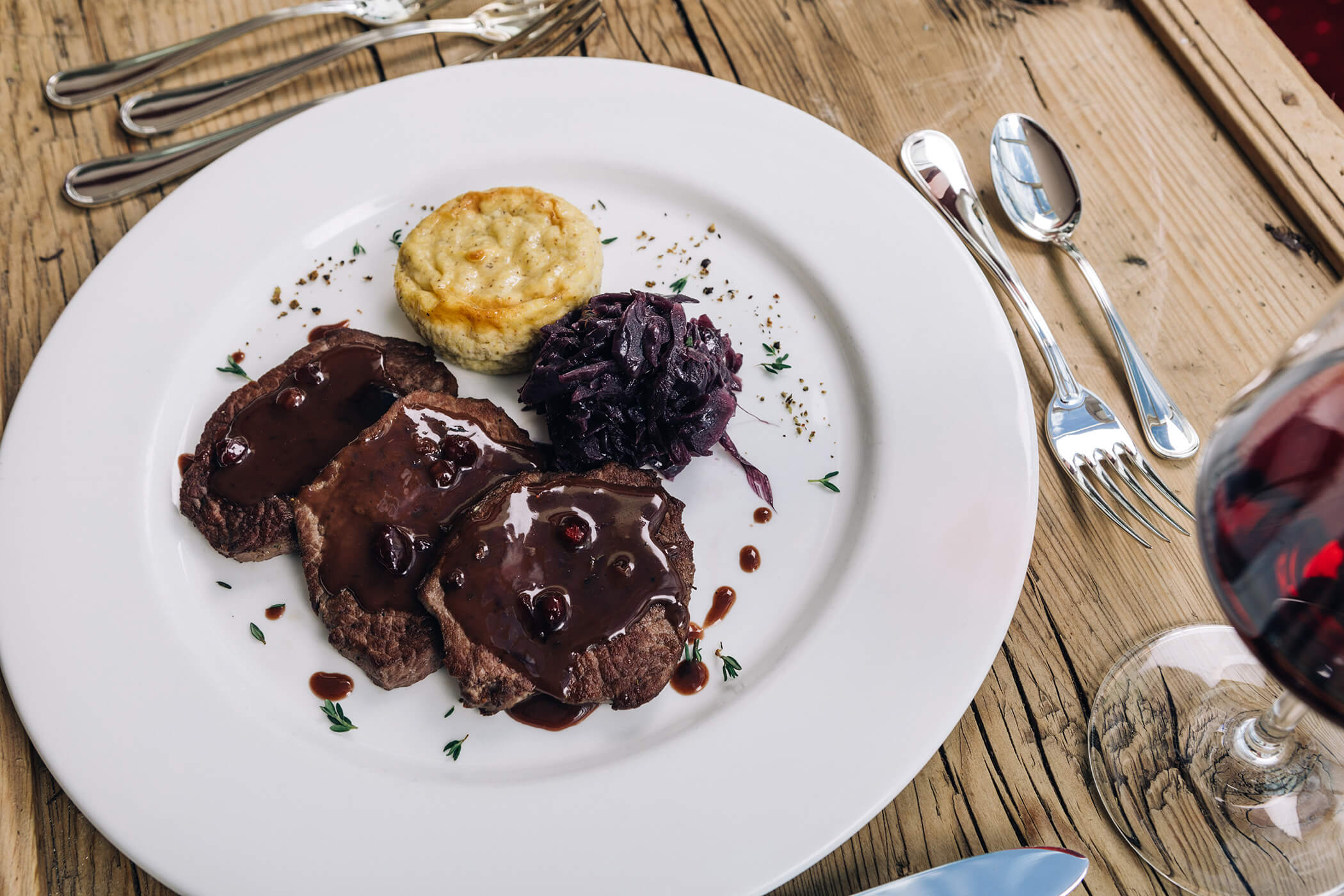 Three slices of roast beef with dark sauce, a potato gratin, and red cabbage on a white plate. - Hotel Tenz