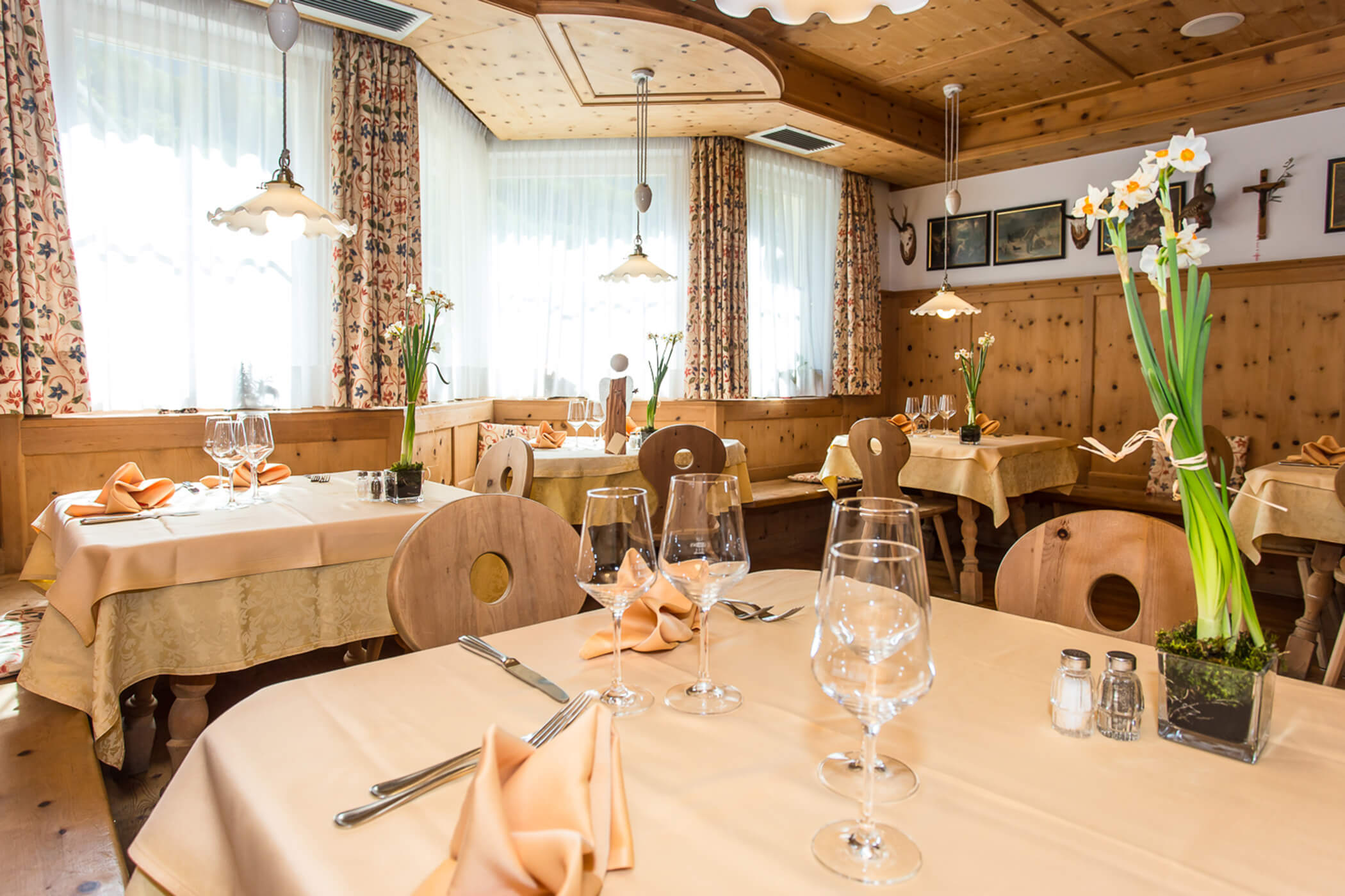 A cozy, sunlit restaurant with wooden decor, set tables, and flowers by the windows. - Hotel Tenz