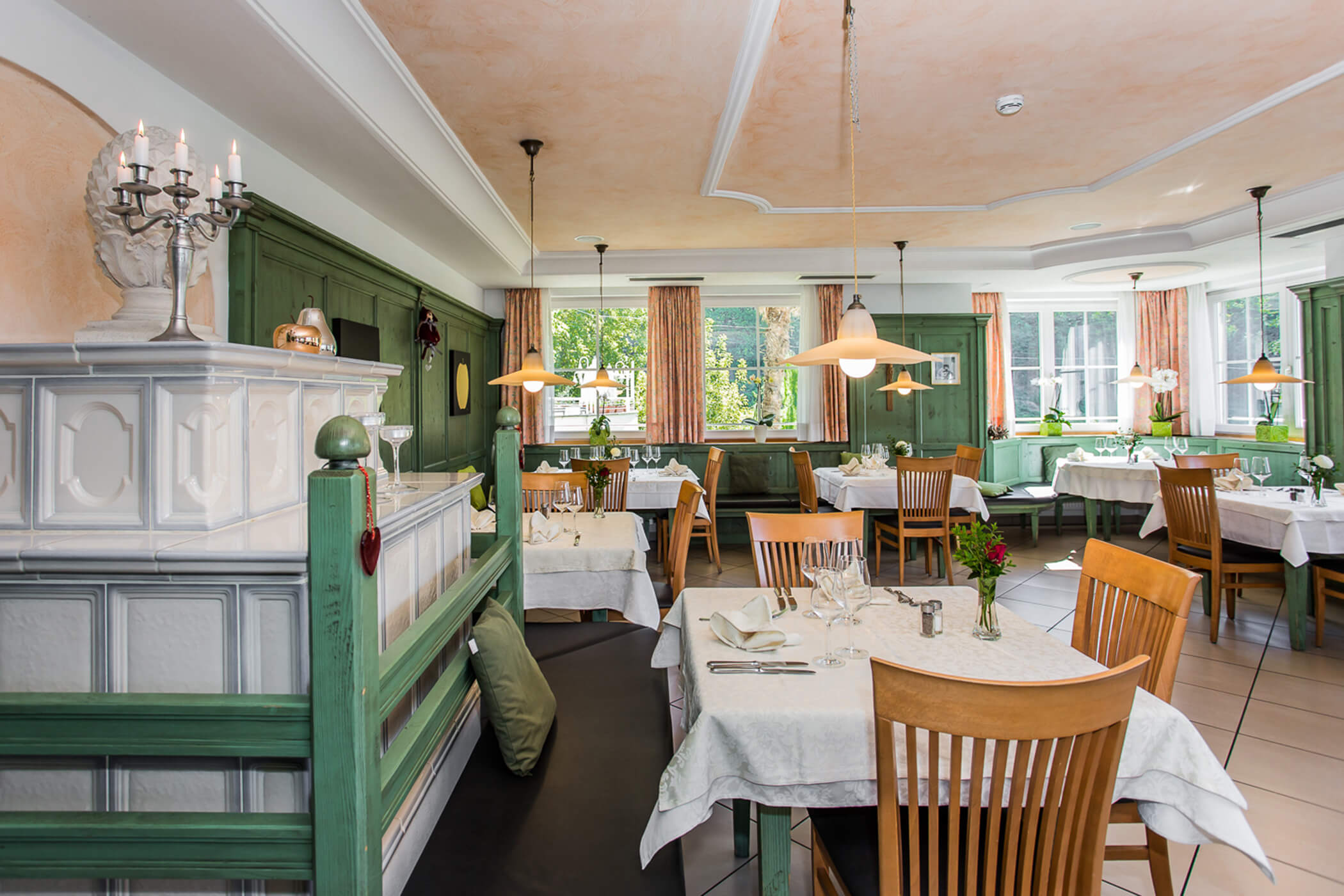 Cozy restaurant interior with green accents, wooden chairs, white tablecloths, and natural light from large windows. - Hotel Tenz