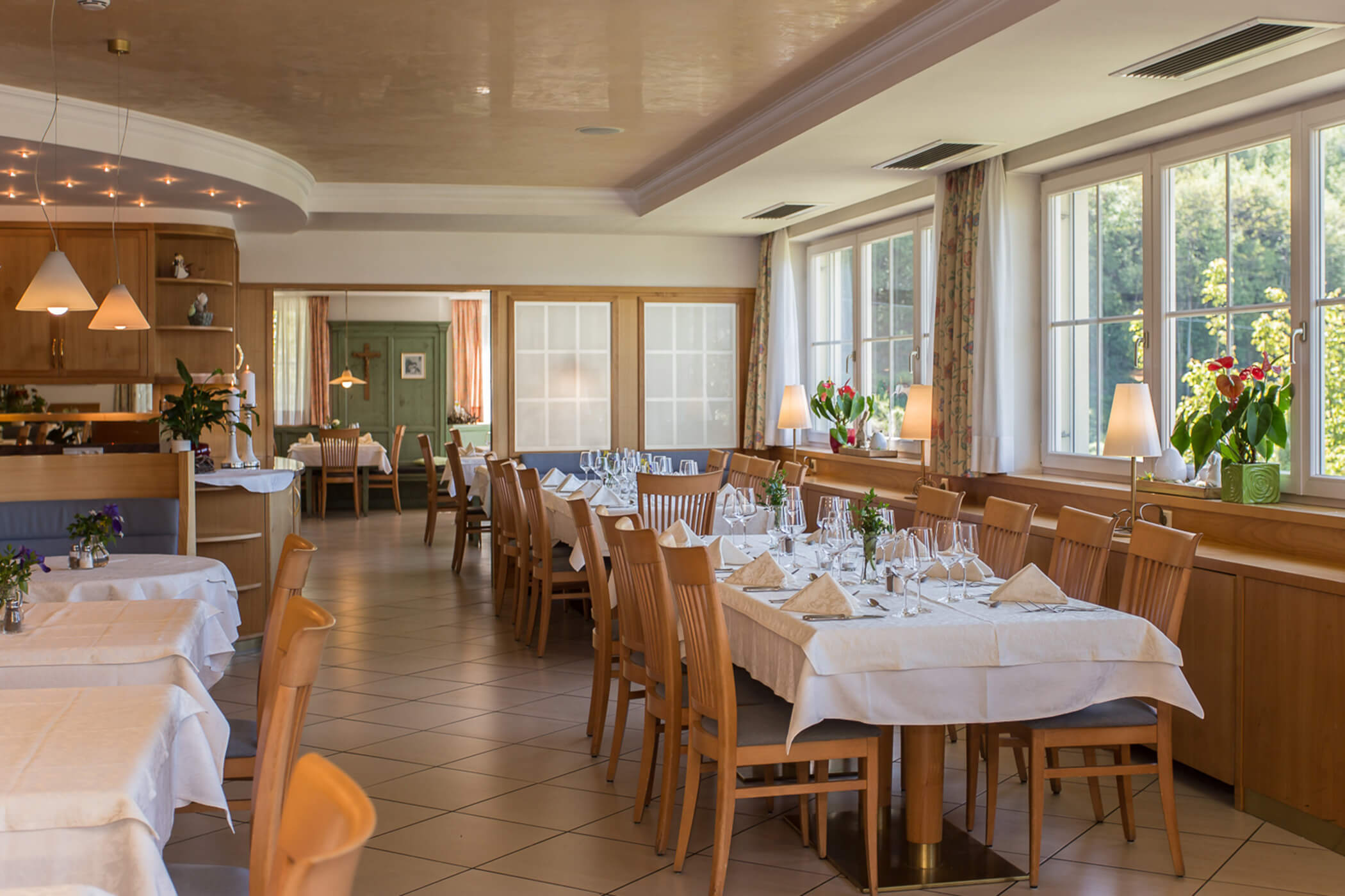 Bright, elegant restaurant dining area with wooden chairs, set tables, and large windows letting in natural light. - Hotel Tenz