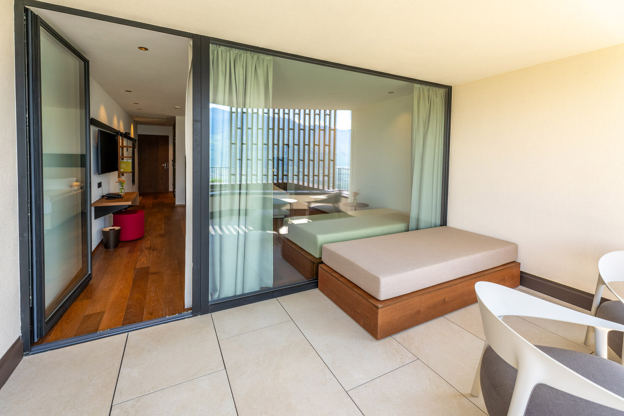 Modern hotel suite with large glass doors, and a patio area with seating and a bench. - Hotel Tenz