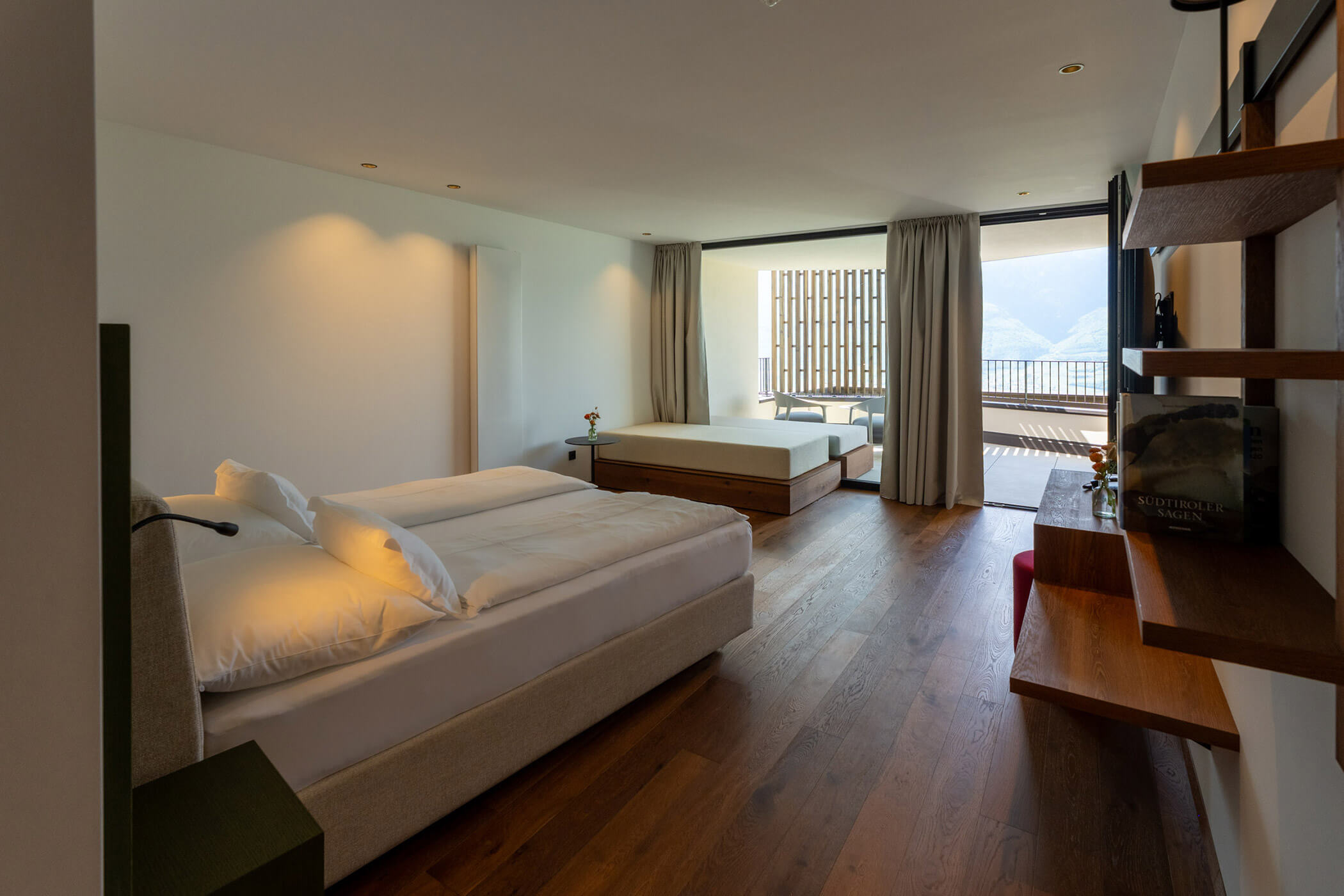 Modern hotel room with two beds, wood floors, a desk, and a balcony with a mountain view. - Hotel Tenz