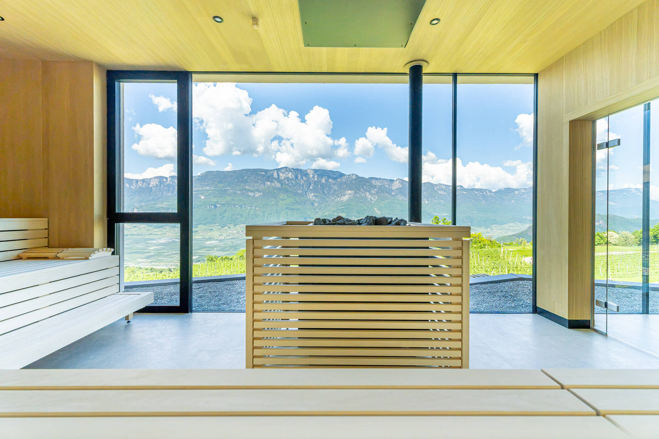 Modern sauna with wooden interior and large window overlooking mountains and a cloudy blue sky. - Hotel Tenz