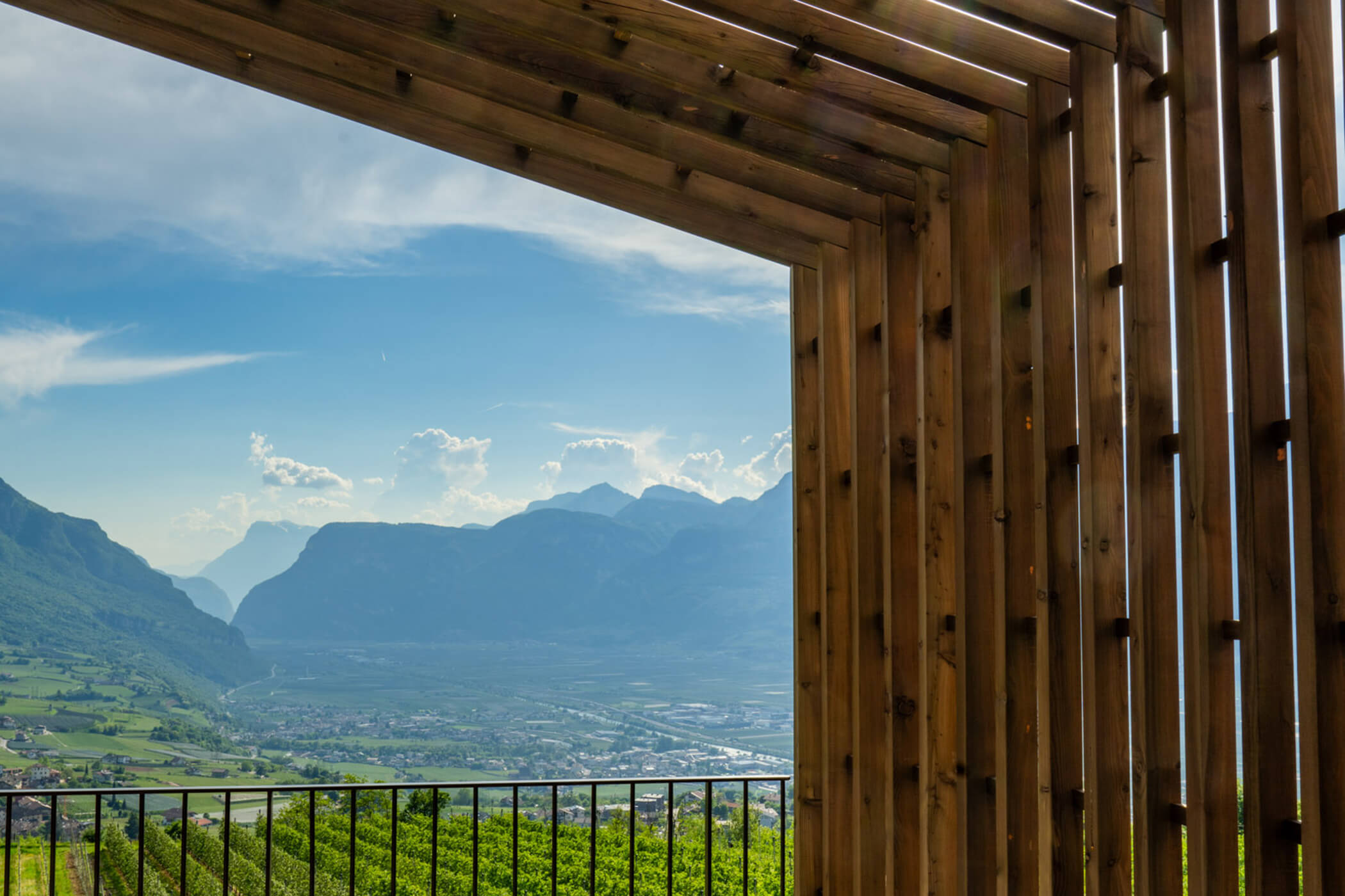 Wooden pergola frames a scenic valley view with mountains, green fields, and a blue sky in the background. - Hotel Tenz